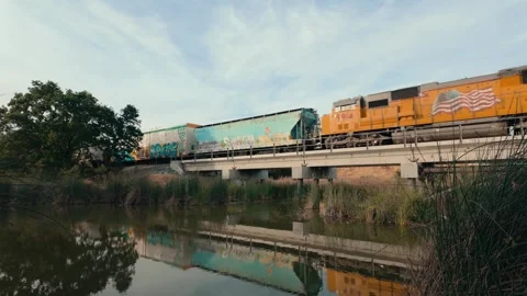 Freight train on bridge over creek at sunset Stock Footage 276853659