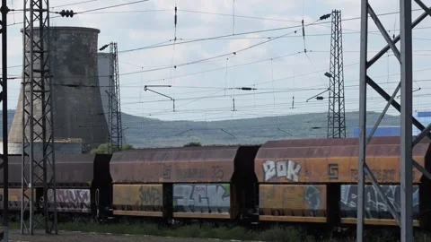 Freight train covered in graffiti transporting goods near a power plant Stock Footage 345928298