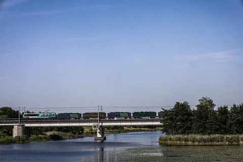 Freight train crosses a bridge over a calm river on a clear day Fotos Stock