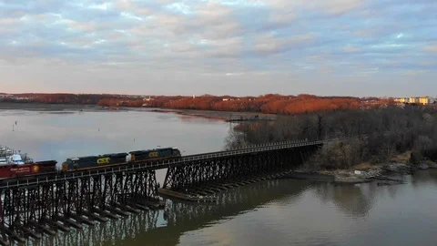 Freight train crossing bridge over river during sunset 動画素材 104011530