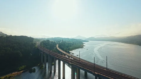 Freight train crossing elevated bridge above wide river under bright sunlight, Stock Footage 340957926