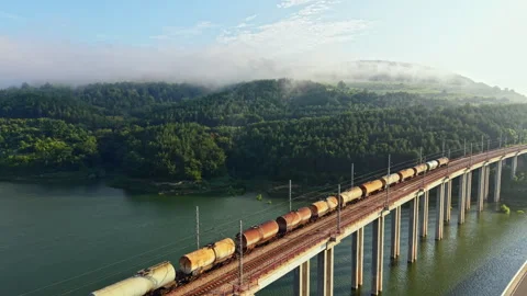Freight train crossing elevated concrete viaduct above wide river, long Stockbeeldmateriaal 341595858