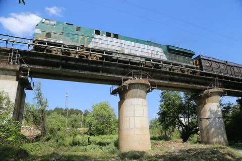 Freight train crossing elevated railway bridge above green landscape under .. Stock Photos