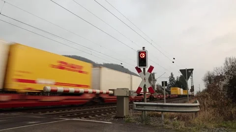A freight train with DHL containers passes a level crossing with closed barrier Stock Footage 257971745
