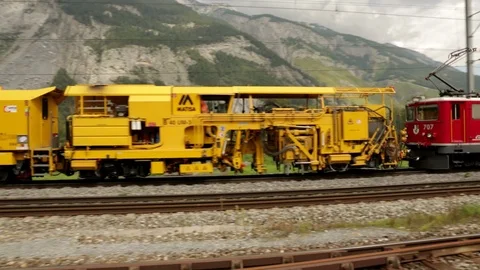 Freight train filled with construction equipment passes camera towards village Stock Footage 86757088