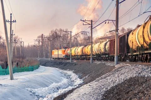 Freight train leaving a bend, trees behind an industrial area, winter evening Stock Photos