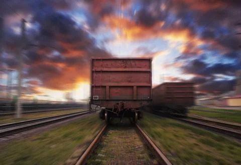 Freight train in motion with blur effect against the sunset sky with clouds. Stock Photos