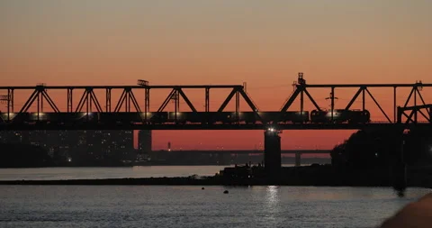 A freight train passes over a bridge over a river at sunset Stock Footage 169424055