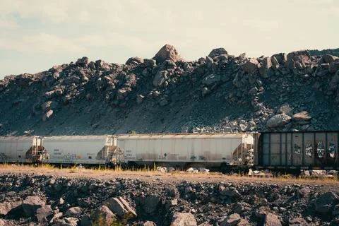 A freight train passes through a rocky landscape, under a cloudy sky. Stock Photos