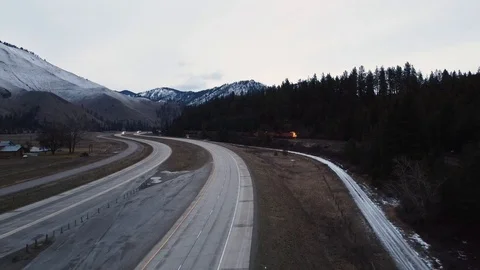Freight train passing along side of open highway with trees and mountain rang Stock Footage 125401689