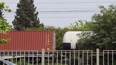 Freight train passing behind fence with tank cars and shipping containers Vidéo 310409231