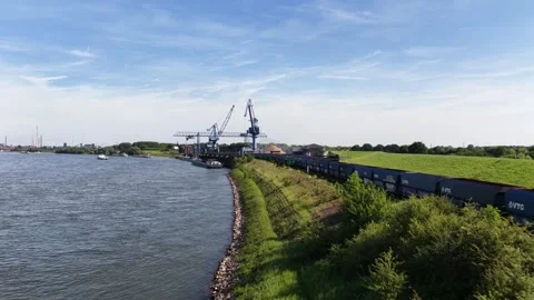 Freight train passing industrial port cranes on riverbank Stock Footage 337448623