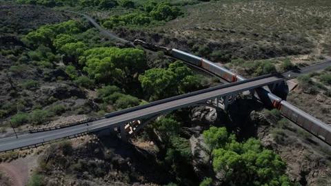 A freight train passing under a bridge in a desert canyon Stock Footage 194851976