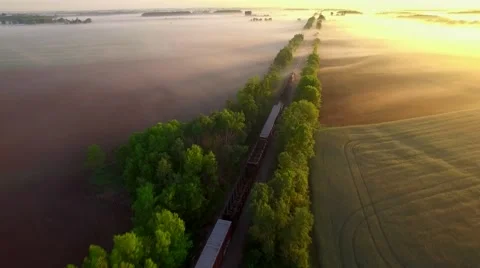 Freight train rolls across peaceful, foggy landscape at sunrise Stock Footage 63476193