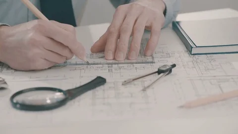 Frellance architect sketching a construction project with pencil and ruler at Stock Footage 75057999