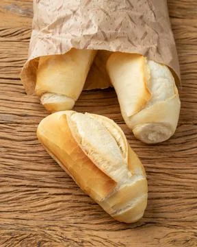 French bread, salt bread or pistolet on a paper bag over wooden table Stock Photos