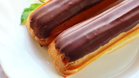 French eclairs with cream filling covered with melted chocolate on a white plate Stock Footage 265247448