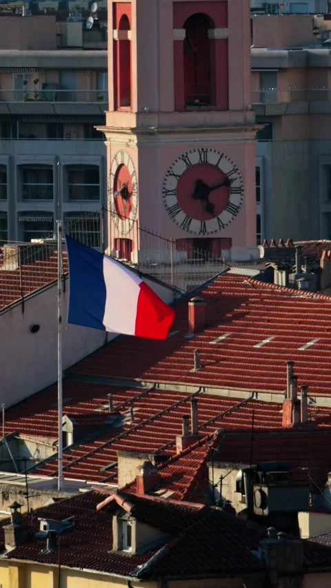 French flag waves gently on flagpole with clock tower and red tiled roofs i.. Stock Footage 339413105