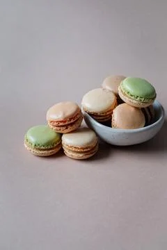 French multicolored mini macarons in a small bowl on beige background Stock Photos