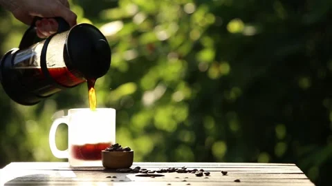French press coffee and cup on table with scattered coffee beans in garden. Stock Footage 147339029