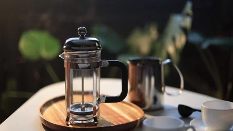 French press coffee maker and milk frothing pitcher on a table with plants in Stock Footage 338990700