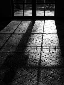 French windows casting dramatic light rays and shadow on the floor tiles. Foto stock