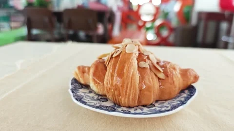 Fresh almond croissant served on a patterned ceramic plate in a cafe. Vídeo Stock 348544841