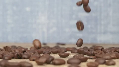 Fresh and aromatic coffee beans cascading beautifully onto a rustic wooden table Видео 288970775