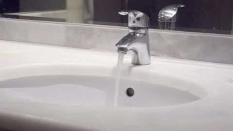 Fresh and clean water flows from a shiny chrome faucet into a marble sink in a Stock Footage 281110281