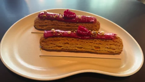 Fresh and delicious eclairs with sweet and sour raspberry cream, served on a Stock Footage 336681860