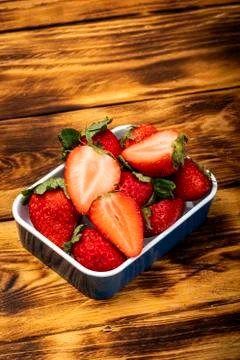 Fresh and split strawberries on rustic wooden table. Stock Photos