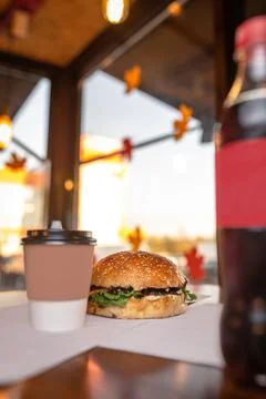 Fresh appetizing burger on the background of coffee and bottles of soda Stock Photos