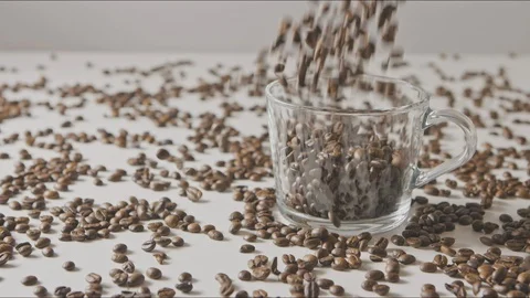Fresh aromatic coffe beans are falling in a glass cup and table. Stock Footage 129631854