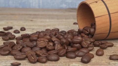 Fresh, aromatic coffee beans spilled dramatically from a rustic wooden container Видео 288970449