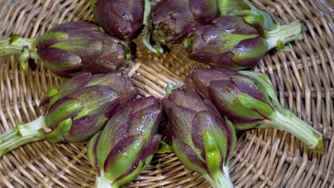 Fresh artichokes in circular composition - rustic straw background - violet a Vidéo 128491739