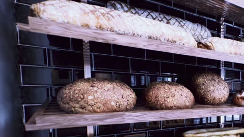 Fresh Artisan Bread Loaves Displayed on Wooden Shelves Inside a Local Bakery Stock Footage 348488100
