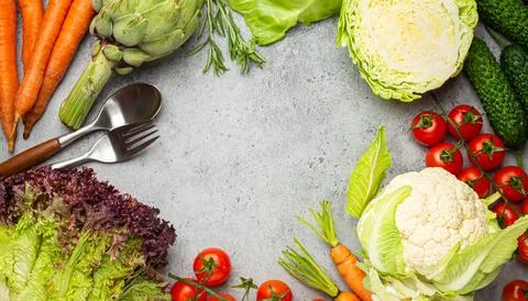 Fresh assorted organic vegetables, spoon, fork on rustic grey stone table t.. Stock Photos