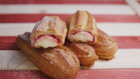 Fresh backed eclairs cookies lying on a red and white striped wooden tray and Video stock 105352841