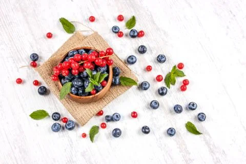 Fresh blueberries and red currants with mint leaves in a wooden bowl on burla Stock Photos