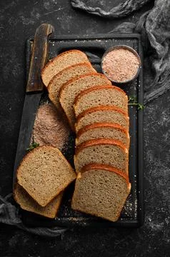 Fresh bran bread. Baking. Top view. Black stone background, rustic style. Stock Photos