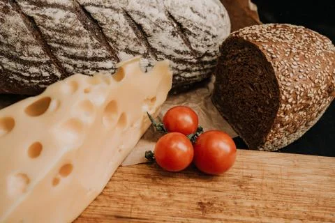 Fresh bread, cherry tomatoes, cheese on wooden black background Stock Photos