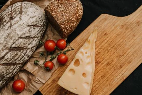 Fresh bread, cherry tomatoes, cheese on wooden black background Stock Photos