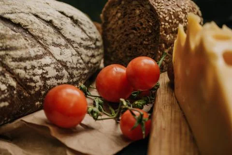 Fresh bread, cherry tomatoes, cheese on wooden black background Stock Photos