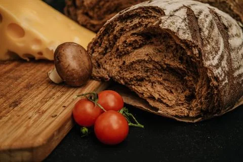 Fresh bread, cherry tomatoes, cheese on wooden black background Stock Photos