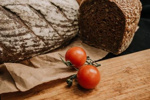 Fresh bread, cherry tomatoes on paper on wooden black background Stock Photos