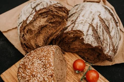Fresh bread, cherry tomatoes on paper on wooden black background Stock Photos