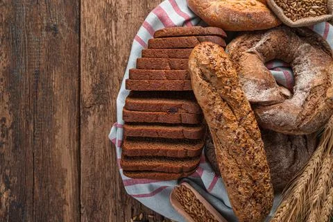Fresh bread of different types, wheat spikelets and grains on a wooden backgr Stock Photos