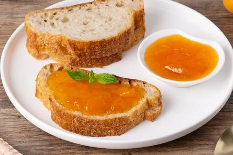 Fresh bread with jam on a plate sitting on a wooden table during breakfast Stock Photos