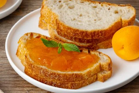 Fresh bread with jam on a plate sitting on a wooden table during breakfast ti Stock Photos