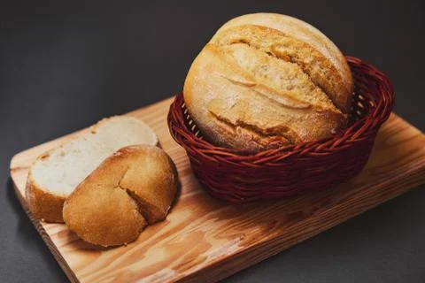 Fresh bread made from wheat flour in a wicker basket made of dark wood lies o Stock Photos